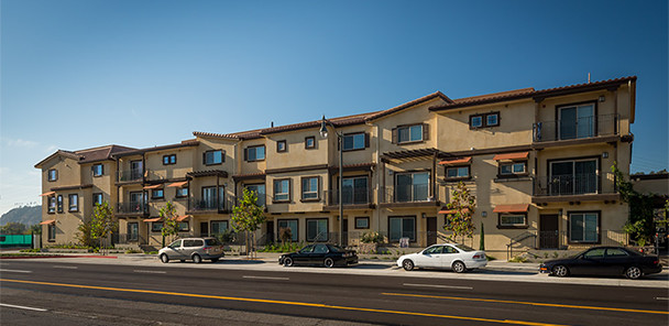 Tree-lined street with with three-story stucco apartment building with tile roof and balconies.